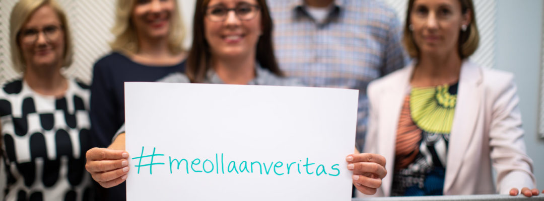 Veritaksen henkilökuntaa. Etualalla olevalla henkilöllä on kyltti kädessä, jossa lukee #meollaanveritas.