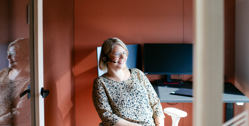 Veritaksen asiakaspalvelija hymyilee puhuessaan puhelimessa kuulokkeilla.