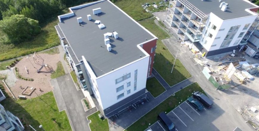 Kesäinen ilmakuva Turun Pryssinkadun kerrostalosta. Kerrostaloa ympäröi nurmialueet sekä lasten leikkipaikka, jossa keinu, hiekkalaatikko ja liukumäki. Talon päädyssä on pyörätelineitä ja autopaikkoja.