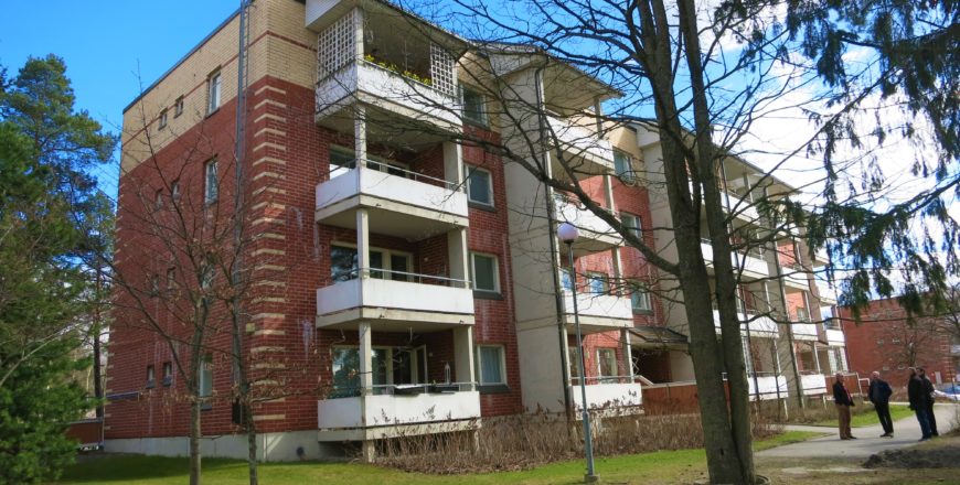 Ulkokuva Espoon Ruutikellarintien kerrostaloasunnoista. Kerrostalo on nelikerroksinen ja väriltään puna-keltainen. Jokaisessa kerroksessa on parvekkeet, jotka ovat väriltään valkoiset. Pihalla on nurmialuetta sekä muutama isompi puu.