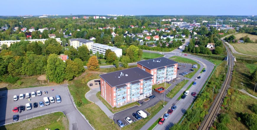 Ilmakuva Turun Raunistulantien asunnoista. Etualalla junaraiteet, tie joka vie kiinteistön pihaan sekä itse kiinteistö, joka on neljäkerroksinen kerrostalo. Kadun varrella on reilusti parkkitilaa. Taaempana näkyy Raunistulaa ja muita alueen asuntoja..