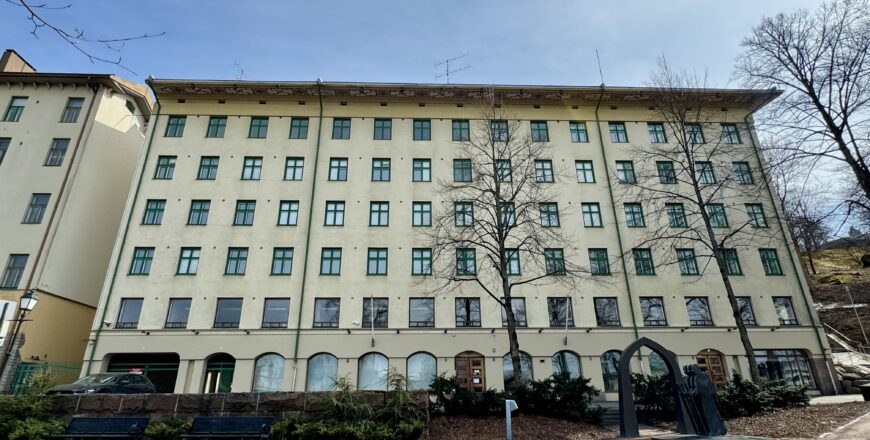 Olavintien kiinteistö kuvattuna etualalta. Rakennus on vaaleankeltainen sekä ikkunoissa on vihreät puitteet.
