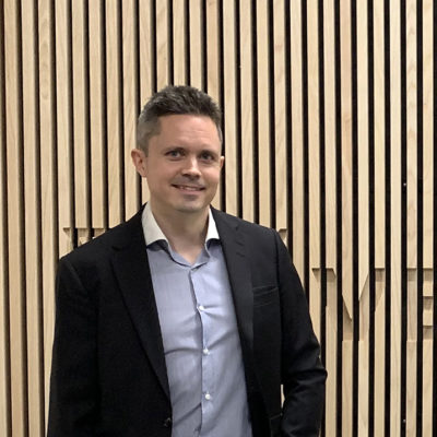 Jussi häkkinen seisoo puisen seinän edessä, jossa lukee "Veritas".