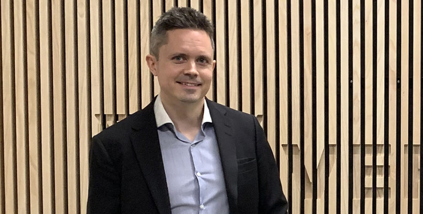 Jussi häkkinen seisoo puisen seinän edessä, jossa lukee "Veritas".