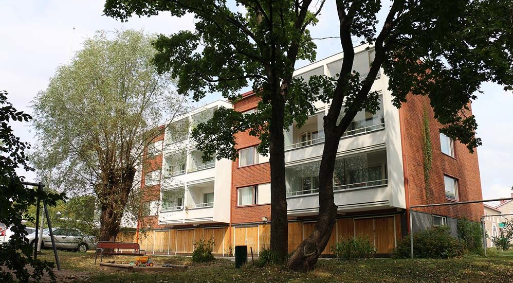 Damaskusvägens flervåningshus i tre våningar fotograferad från baksidan. Det finns en sandlåda för barn, en bänk och parkeringplats på bakgården.