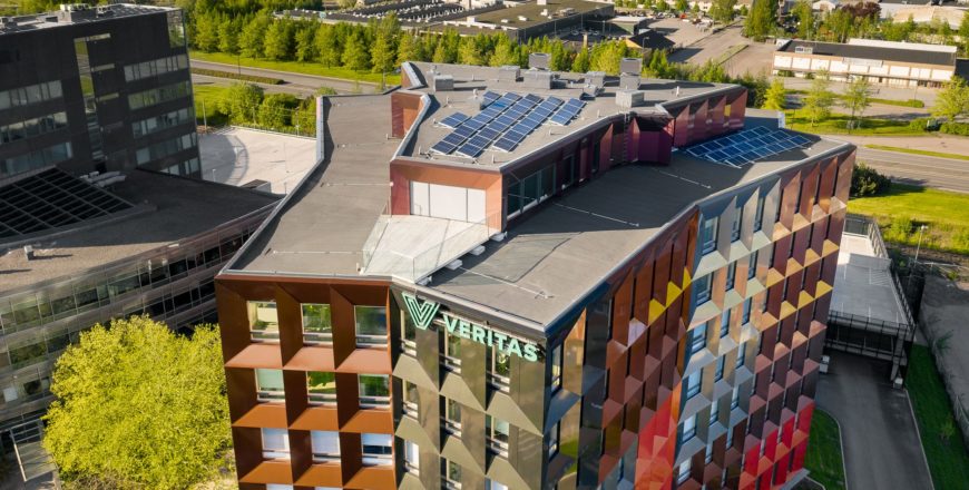 Kesäinen ilmakuva Veritaksen värikkäästä pääkonttorista, Retoriikasta, jonka katolla on kymmeniä aurinkopaneeleja. Taustalla näkyy Helsingin valtatie ja sen takana olevia muita kiinteistöjä.