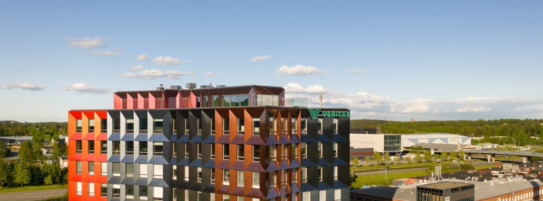 Ilmakuva Veritaksen pääkonttori Trivium Retoriikasta. Kesäinen kuva, jossa etualalla monivärinen Retoriikka. Taustalla sininen taivas, kasvillisuutta sekä lähirakennuksia. Talon takana kulkee Helsingin valtatie.
