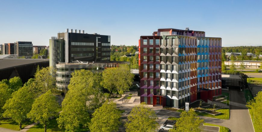 Kupittaanpuiston suunnalta kuvattu Veritaksen pääkonttori Trivium Retoriikka. Kuva on kesäisen vehreä, rakennus on monivärinen ja sen edessä on parkkitilaa.