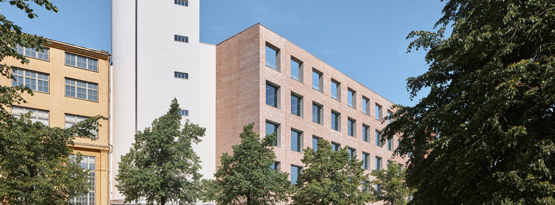 Aurinkoisena päivänä etäältä kuvatut Helsingin taideyliopiston rakennukset. Rakennusten etupuolella on rivistö puita ja muutama ohikulkija.