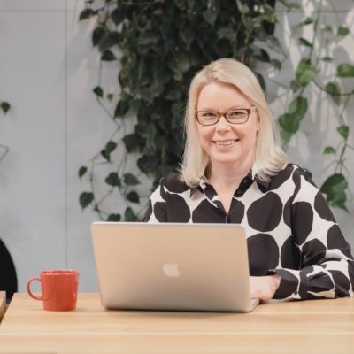 Yrittäjä Tuuli Ilves istuu tietokoneen edessä ja hymyilee kameraan.