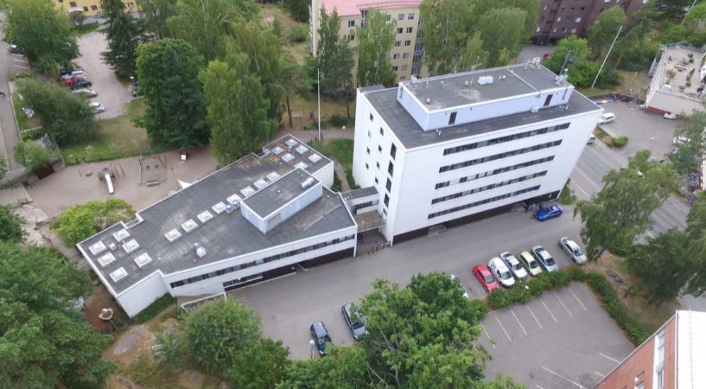Flygfoto av Bostads Ab Sjöalléns flervåningshus. I förgrunden finns parkeringsplatser och bakom huset finns andra flervåningshus.