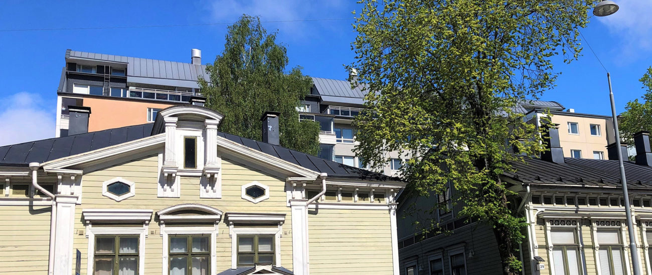 Linnankadun asuintalojen julkisivukuva. Kerrostalo on taka-alalla ja sen edessä vihreät puutalot, joiden välistä on portti sisäpihalle. Talojen edessä on mahdollista pysäköidä.