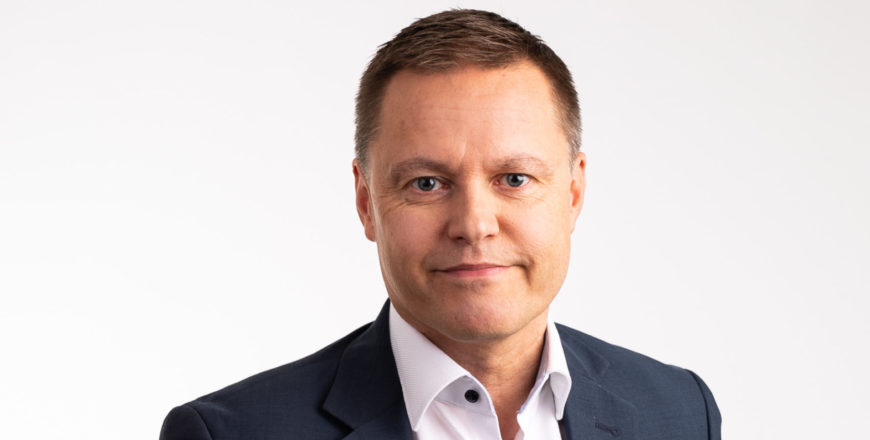 Henkilö seisoo ja hymyilee kameralle.