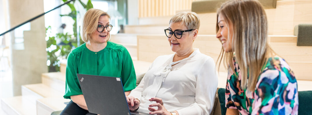Kolme Veritaksen työntekijää istuu penkillä tietokoneen ääressä pääkonttorilla Turussa.