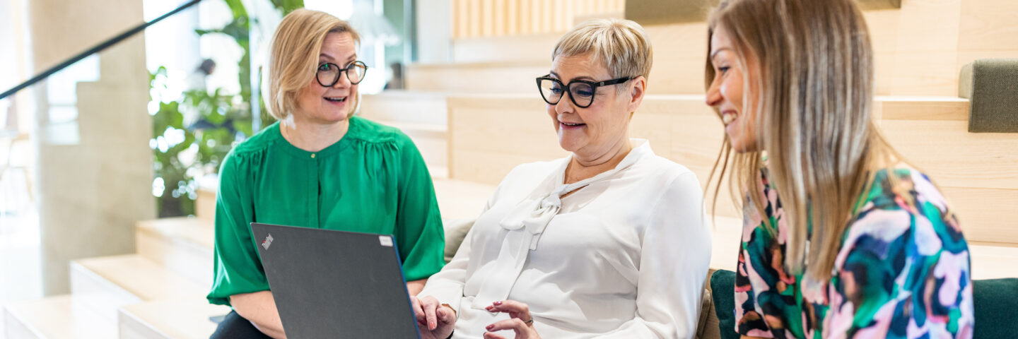 Kolme Veritaksen työntekijää istuu penkillä tietokoneen ääressä pääkonttorilla Turussa.