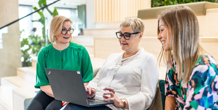 Kolme Veritaksen työntekijää istuu penkillä tietokoneen ääressä pääkonttorilla Turussa.